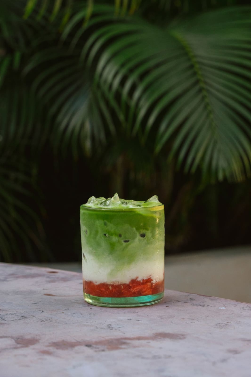 A layered strawberry matcha in a glass tumbler against a palm.