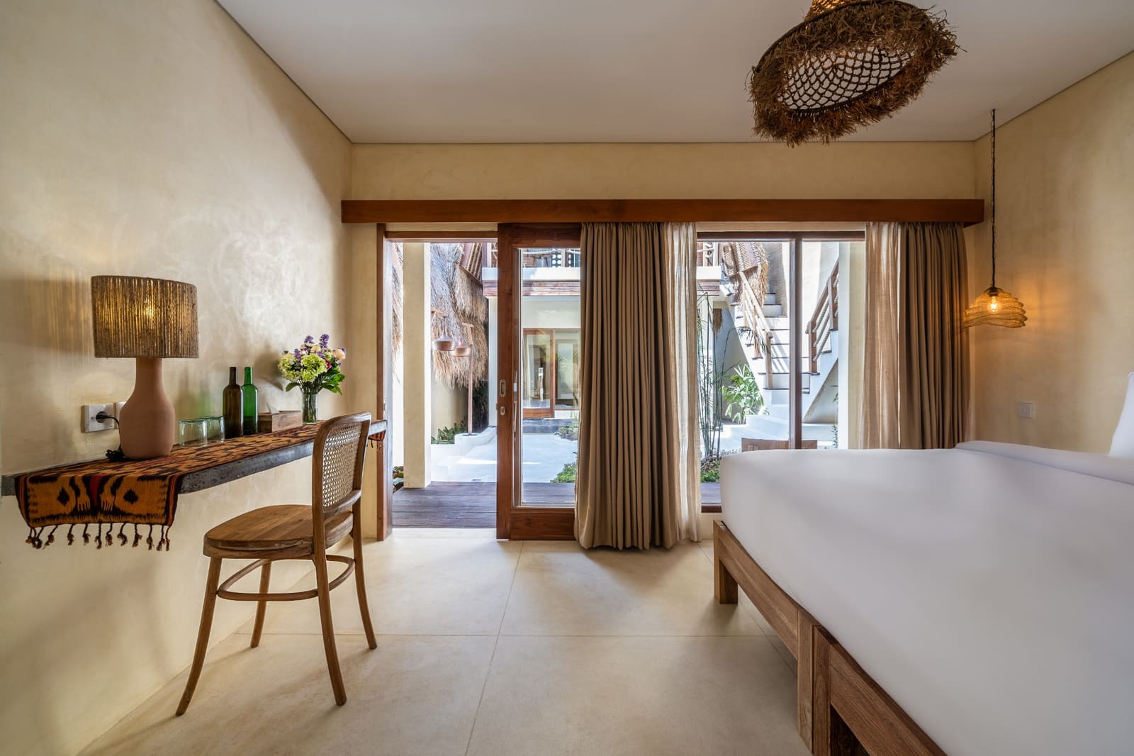 A room looking out through sliding doors to the courtyard, with a long desk and woven lamps.