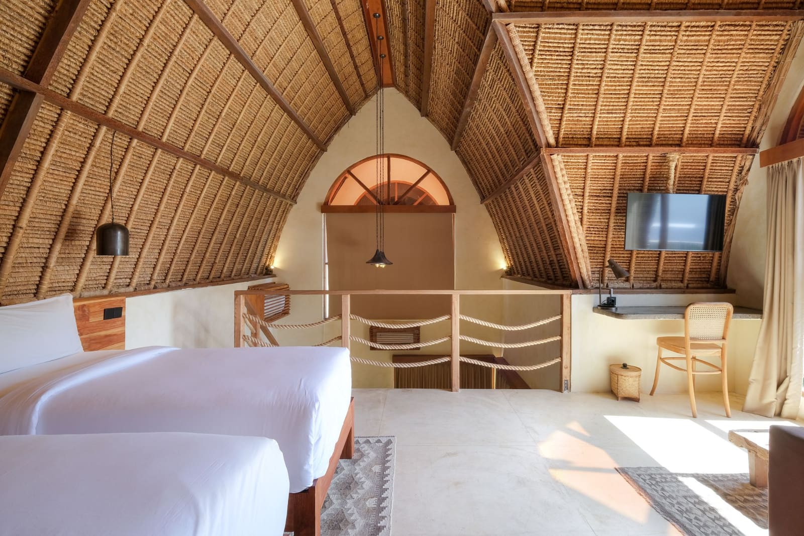 A room at Lulu's: a vaulted alang-alang roof over two beds, a mezzanine rail and a desk by the window.